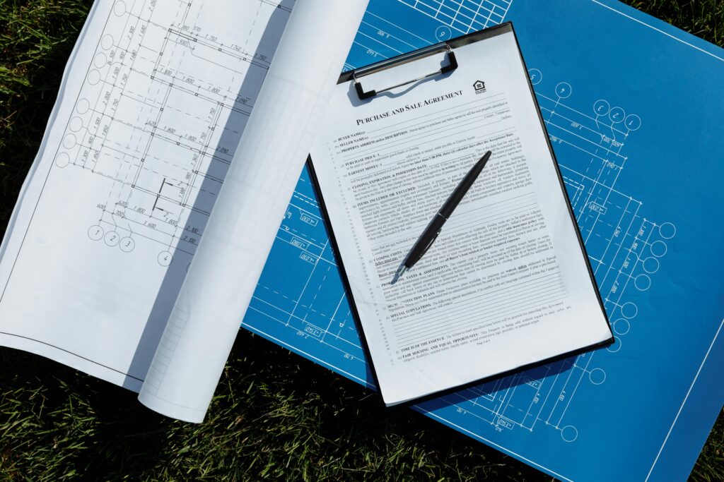 Overhead view of architectural blueprints and a contract with pen on grass, ideal for real estate and construction themes.